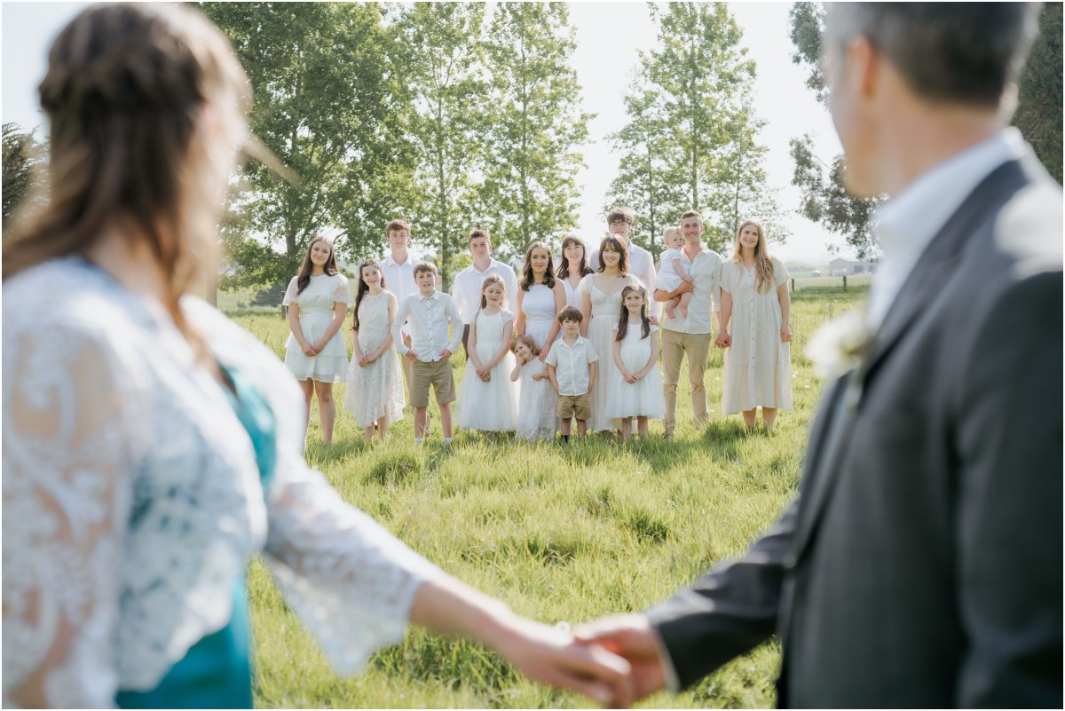 Candid family portrait photography in Timaru: Large extended family group dressed in white posing together on a lush green lawn.