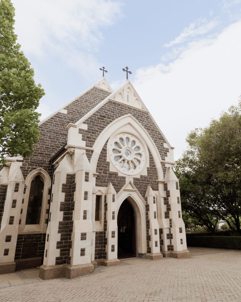 The striking stone exterior architecture of the historic Rose Chapel in Christchurch against a bright blue sky.