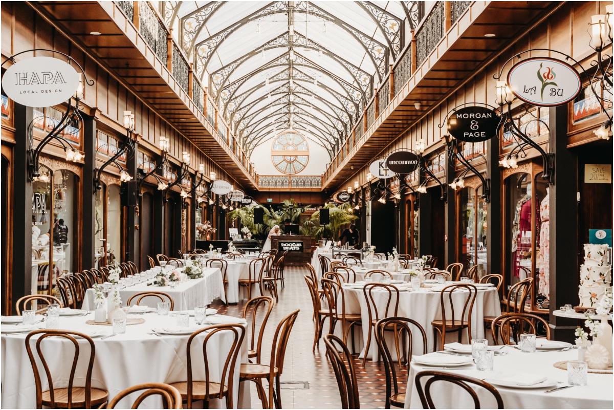 The Tannery wedding reception atrium in Christchurch: Ornate Victorian glass atrium roof showcasing elegant reception tables setups and bentwood chairs.
