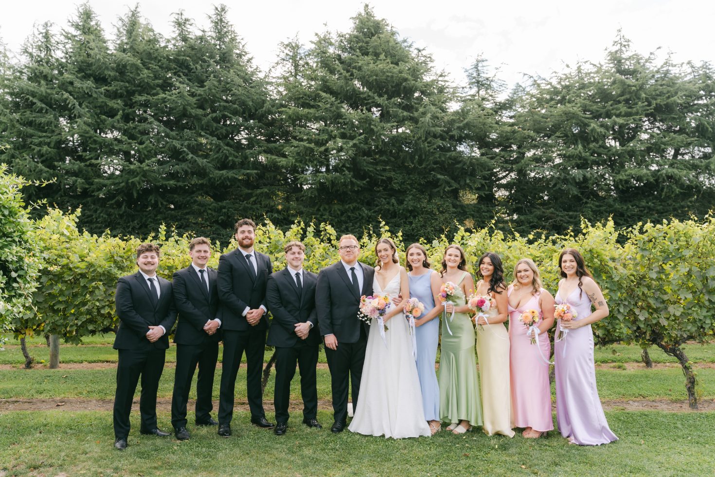 Full bridal party posing together on the lawn in front of lush vineyard hedges in Canterbury.