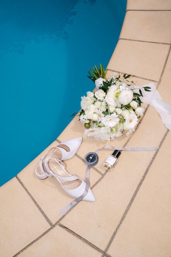 Canterbury wedding details: Fresh white rose bouquet, silk ribbons, and perfume styled by a swimming pool edge by Agnes Grace.