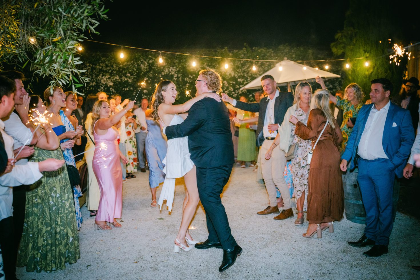 Magical wedding sparkler exit at Cossars Wineshed: Blair and Ben laughing as they walk through a tunnel of glowing sparks in the courtyard.