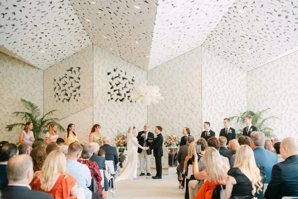 Fine art Christchurch wedding photography: Wide indoor ceremony framed beneath a modern geometric ceiling structure.