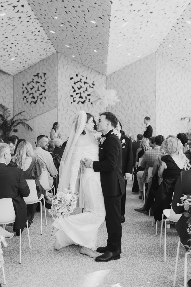 Charlotte and Kiril cheering with raised arms as they walk back down the aisle together as husband and wife.
