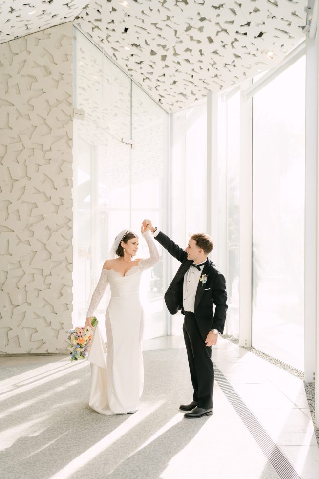 The Ilex Hagley Park wedding: Newlyweds holding hands and celebrating down the indoor white event space.
