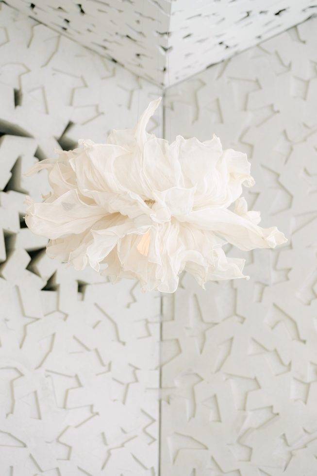 Detail close-up of a large white statement floral installation hanging against the unique textured walls of The Ilex Café.