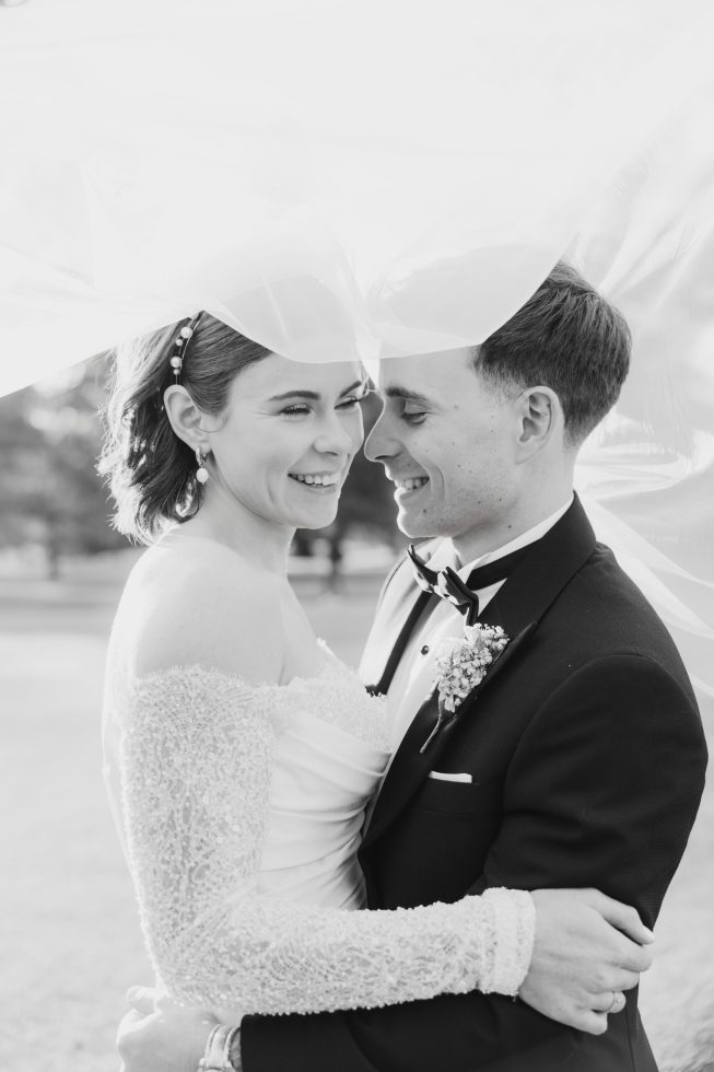Black and white wedding portrait: Romantic close-up profile of Charlotte and Kiril sharing a smile under a tulle veil.