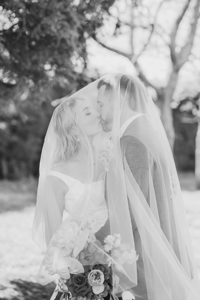 Black and white wedding photography: Romantic close up of a couple kissing under a sheer tulle wedding veil in Timaru, NZ.