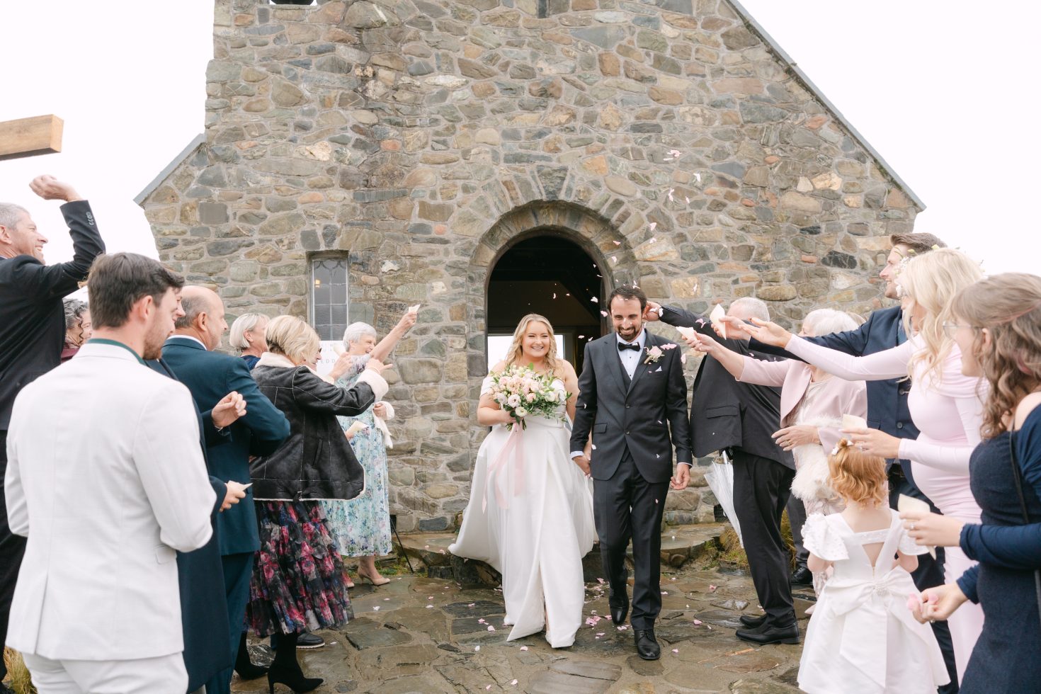 A bride and groom walking out of the stone archway during a Church of the Good Shepherd wedding confetti exit.