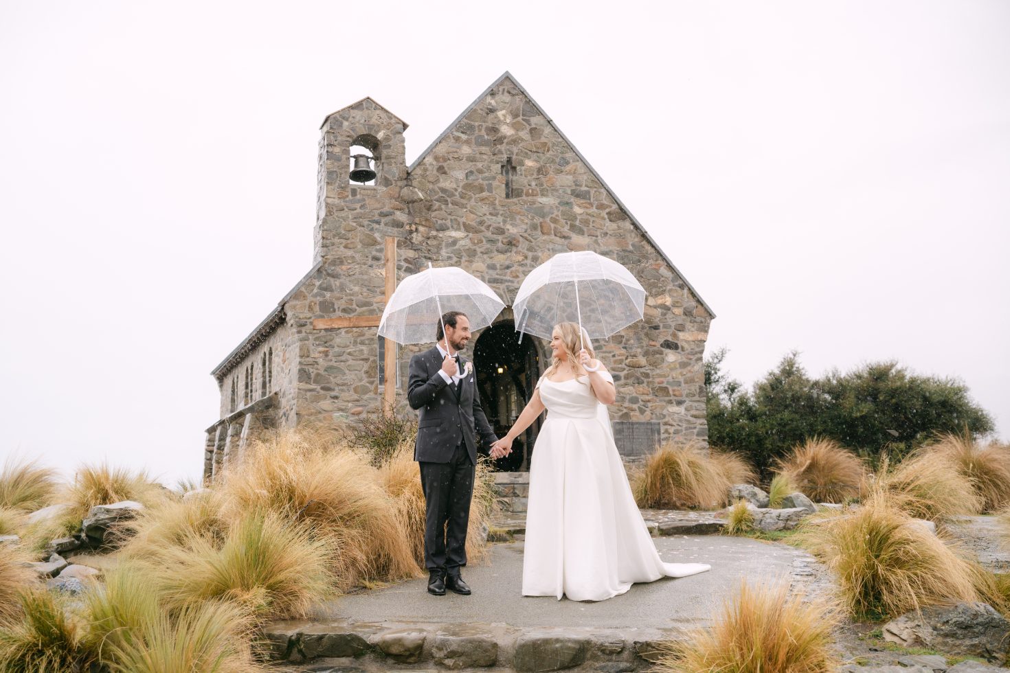 A bridal party standing with umbrellas by the bell tower for a winter Church of the Good Shepherd wedding elopement.
