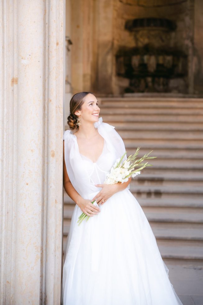 Fine art bridal portrait: Soft, close-up profile of a bride holding flowers inside a historic European castle.