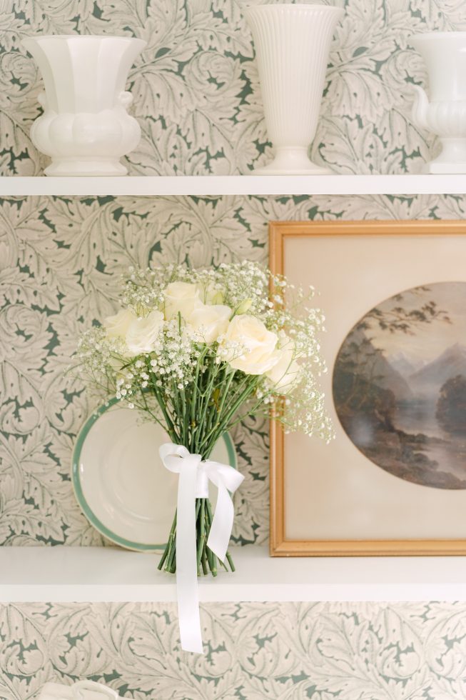 Ashburton wedding photography: Classic white bridal bouquet set against elegant textured wallpaper during preparation.