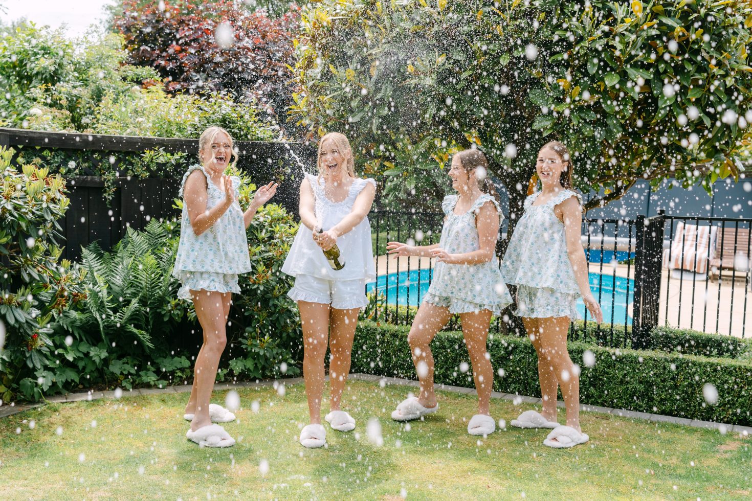 The bridal party in matching getting-ready sets laughing and celebrating outdoors by the pool.