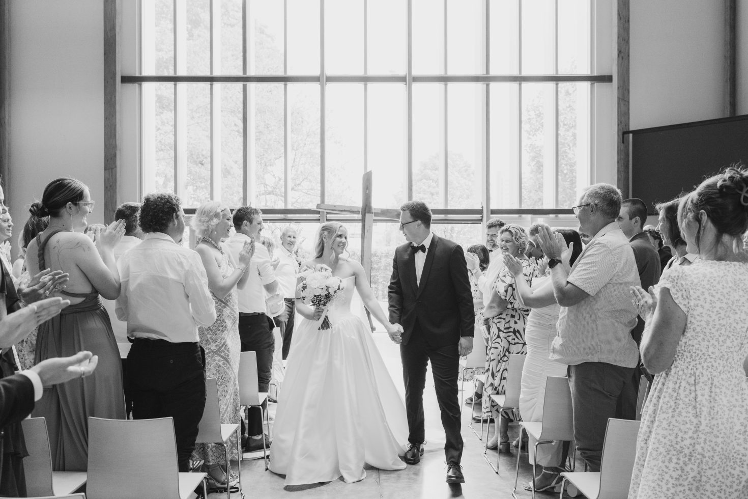 Black and white candid photo of guests cheering as Annabelle and Caleb walk down the aisle as husband and wife.