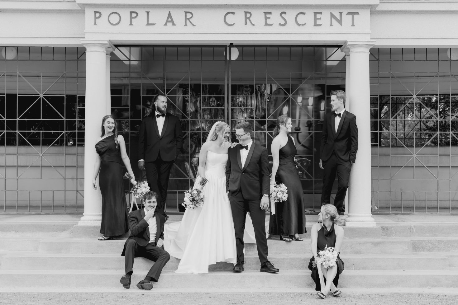 Black and white wide shot of the entire wedding party assembled under the Poplar Crescent entrance.